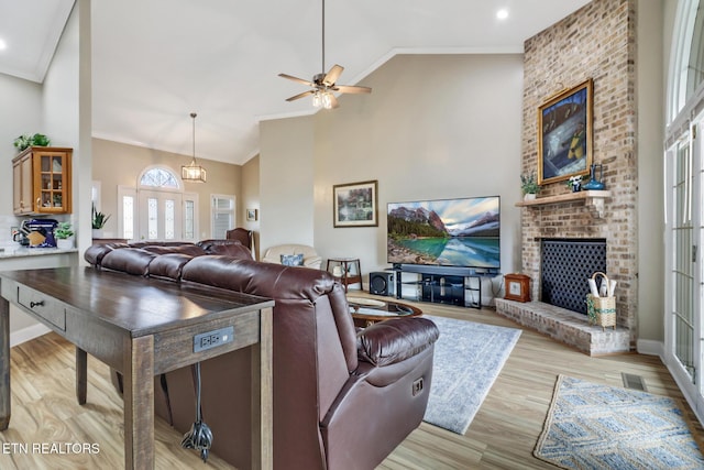 living room featuring a fireplace, ornamental molding, high vaulted ceiling, and light wood-type flooring