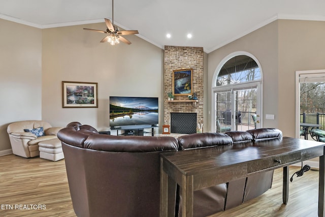 living room with light hardwood / wood-style flooring, ceiling fan, high vaulted ceiling, a fireplace, and ornamental molding