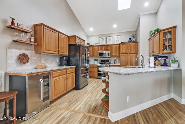 kitchen with sink, ornamental molding, appliances with stainless steel finishes, kitchen peninsula, and light stone countertops