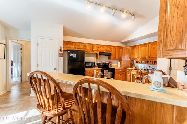 kitchen with vaulted ceiling, kitchen peninsula, a kitchen bar, and black appliances