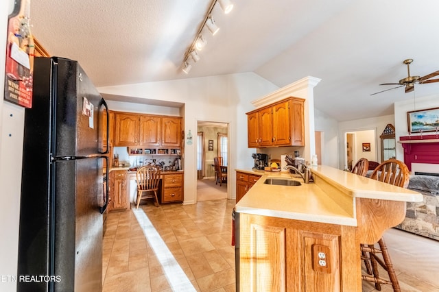 kitchen featuring lofted ceiling, sink, a breakfast bar area, black refrigerator, and kitchen peninsula