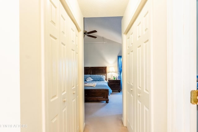 hall with vaulted ceiling, light colored carpet, and a textured ceiling