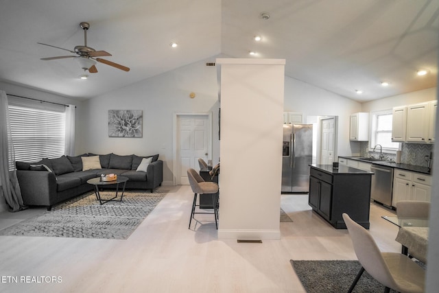 living room featuring ceiling fan, high vaulted ceiling, sink, and light wood-type flooring