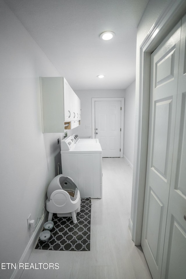 laundry room with cabinets, washing machine and clothes dryer, and light hardwood / wood-style flooring