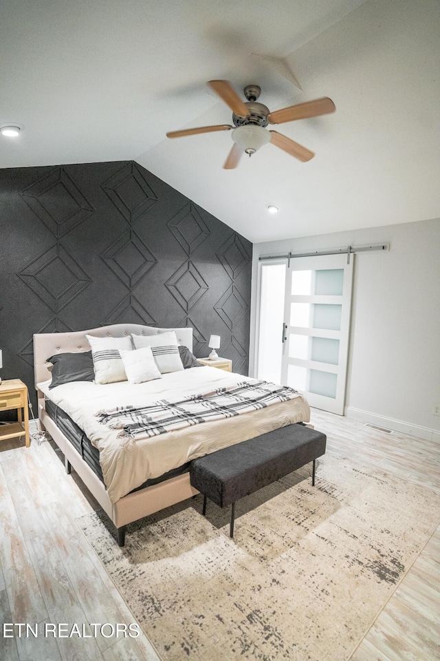 bedroom featuring a barn door, lofted ceiling, ceiling fan, and light hardwood / wood-style flooring