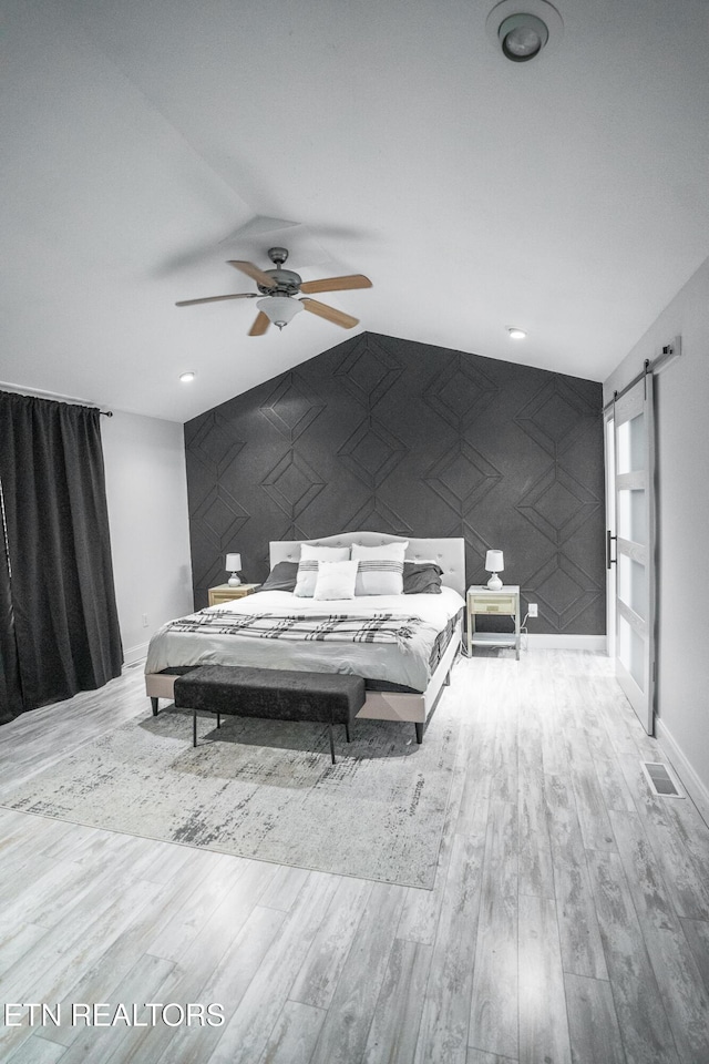 bedroom with light hardwood / wood-style floors, a barn door, and ceiling fan