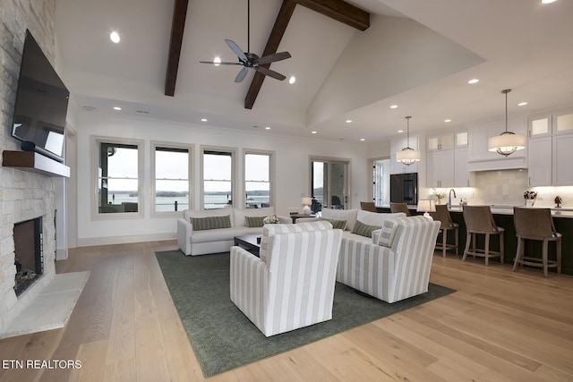 living area featuring high vaulted ceiling, a stone fireplace, wood finished floors, beam ceiling, and crown molding