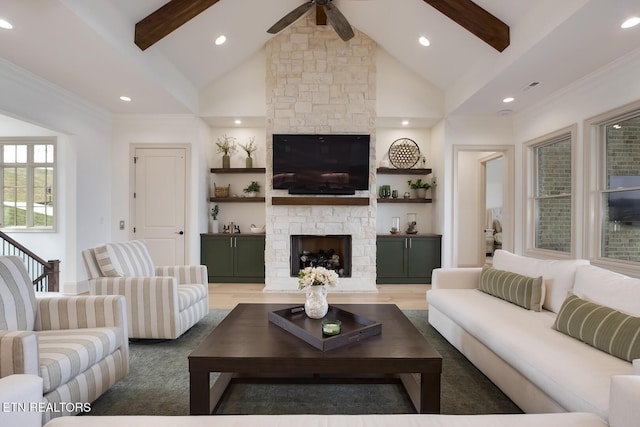 living room with ceiling fan, a stone fireplace, wood finished floors, high vaulted ceiling, and beamed ceiling