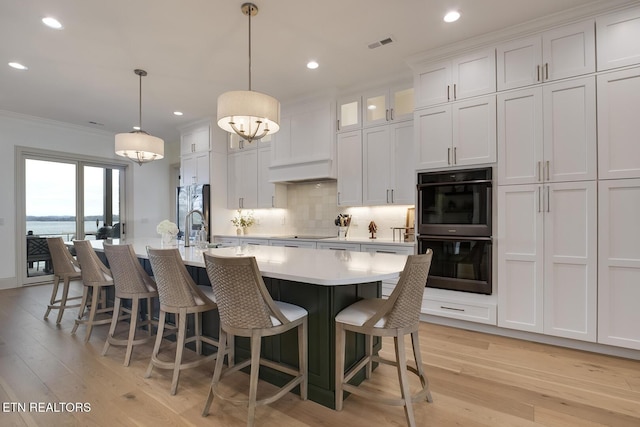 kitchen featuring an island with sink, glass insert cabinets, black appliances, white cabinetry, and pendant lighting