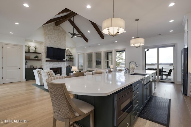 kitchen featuring stainless steel microwave, decorative light fixtures, a kitchen island with sink, light countertops, and a sink