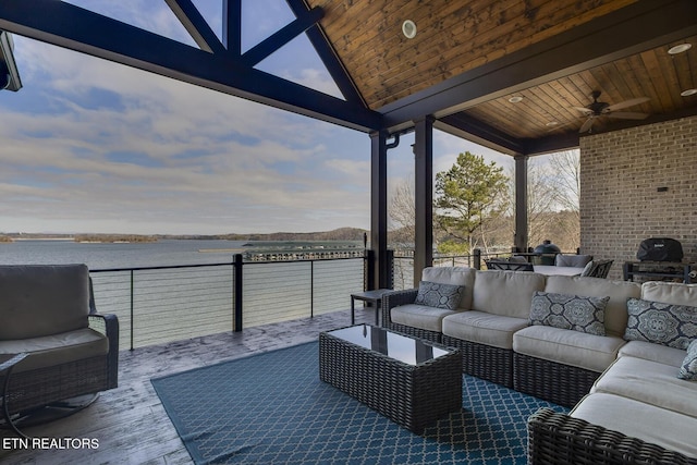 patio terrace at dusk with a water view, ceiling fan, outdoor lounge area, and grilling area