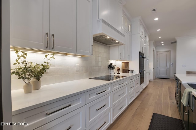 kitchen with white cabinetry, light countertops, decorative backsplash, black appliances, and light wood finished floors