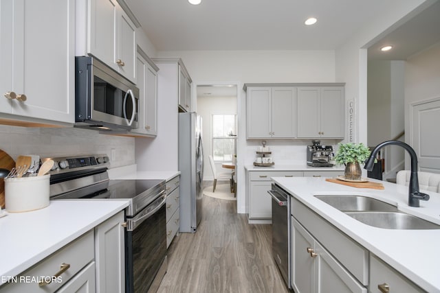 kitchen featuring tasteful backsplash, sink, gray cabinetry, stainless steel appliances, and light wood-type flooring