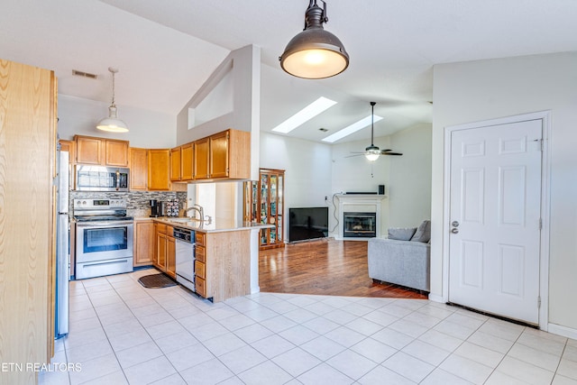 kitchen with pendant lighting, lofted ceiling with skylight, stainless steel appliances, light tile patterned flooring, and kitchen peninsula