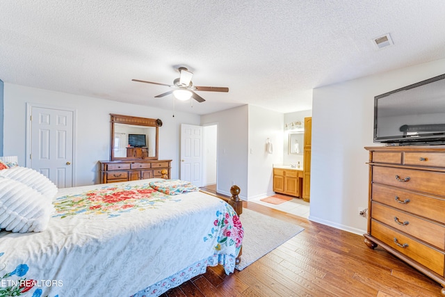 bedroom featuring ceiling fan, ensuite bathroom, a textured ceiling, and light wood-type flooring