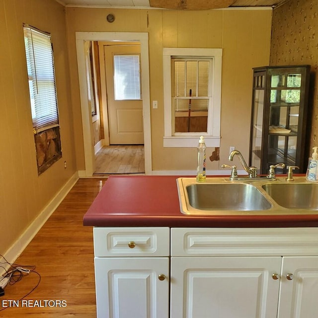 kitchen featuring white cabinetry, sink, wood walls, and light wood-type flooring