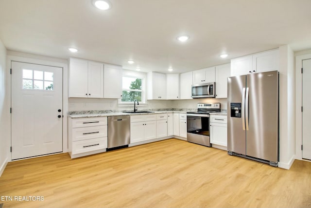 kitchen featuring sink, light hardwood / wood-style flooring, appliances with stainless steel finishes, white cabinetry, and light stone counters