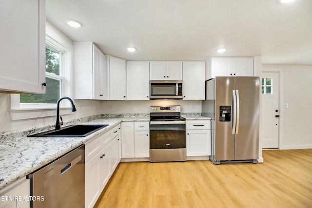 kitchen with white cabinetry, sink, light stone counters, stainless steel appliances, and light hardwood / wood-style flooring