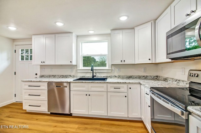 kitchen featuring sink, appliances with stainless steel finishes, light stone countertops, white cabinets, and light wood-type flooring