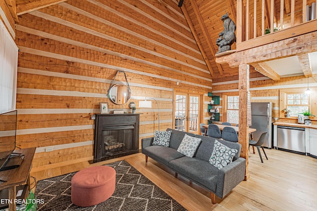 living room with vaulted ceiling, light wood-type flooring, french doors, and wood walls