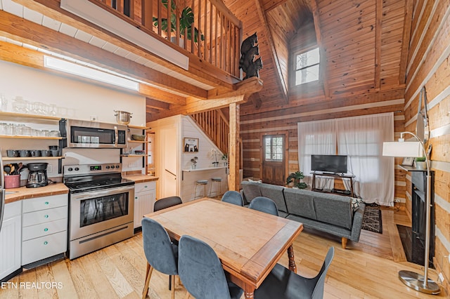 kitchen with appliances with stainless steel finishes, wood walls, white cabinetry, a high ceiling, and light hardwood / wood-style flooring