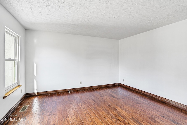 empty room with a textured ceiling and dark hardwood / wood-style flooring