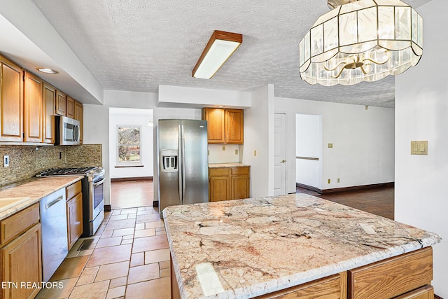 kitchen with decorative backsplash, hanging light fixtures, stainless steel appliances, light stone countertops, and a textured ceiling