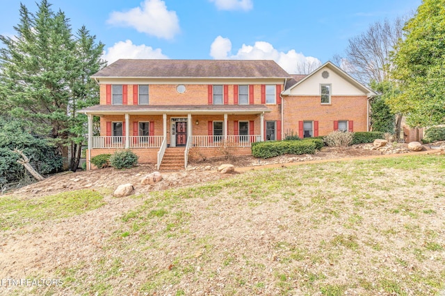 colonial house featuring brick siding, covered porch, and a front lawn