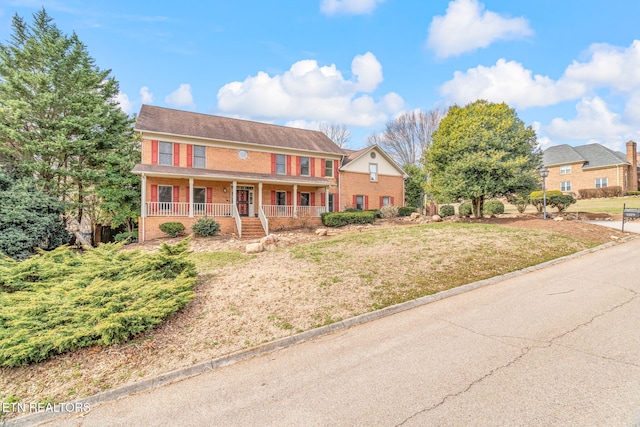 colonial home with a front yard, brick siding, and covered porch