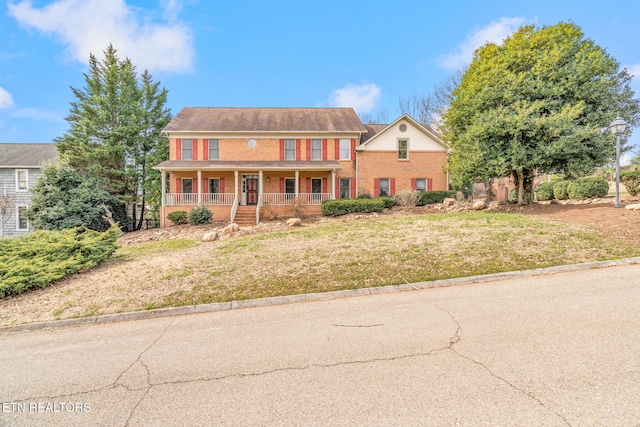 colonial inspired home featuring brick siding, a porch, and a front lawn