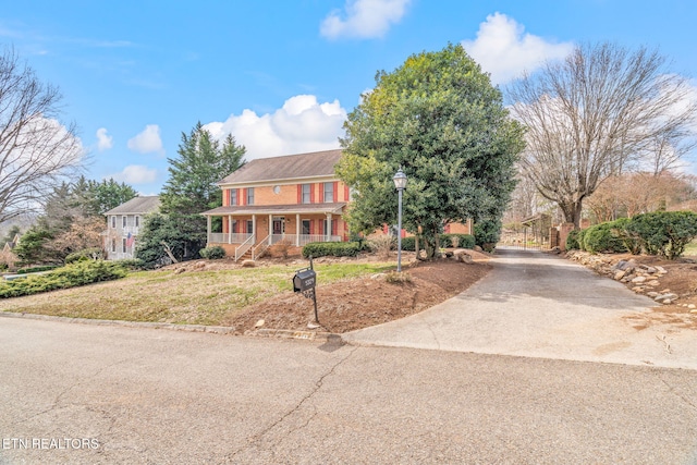 colonial-style house featuring covered porch, concrete driveway, a front yard, and a gate