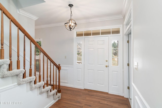 foyer with stairway, a wainscoted wall, dark wood finished floors, an inviting chandelier, and crown molding