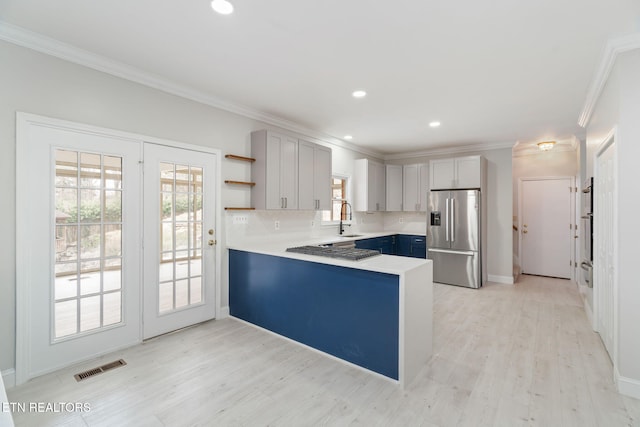 kitchen featuring a sink, backsplash, a peninsula, stainless steel appliances, and open shelves