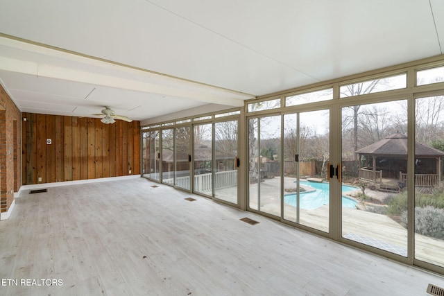 unfurnished sunroom with visible vents, a healthy amount of sunlight, and ceiling fan