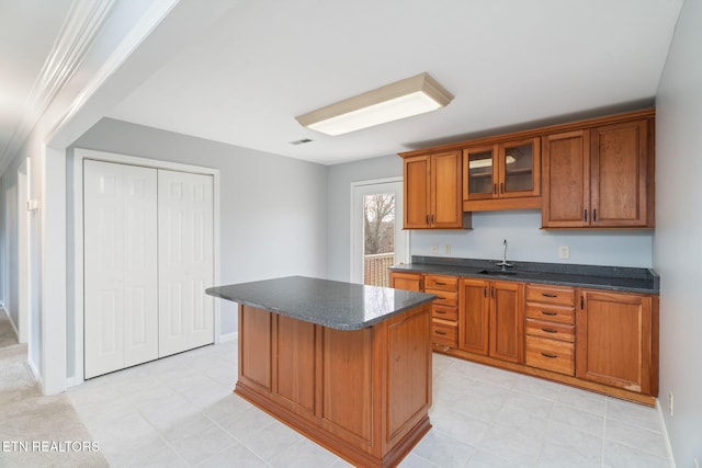 kitchen featuring visible vents, a kitchen island, glass insert cabinets, brown cabinetry, and a sink