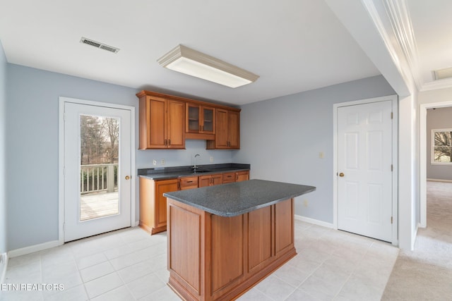 kitchen with visible vents, a sink, a kitchen island, dark countertops, and brown cabinetry