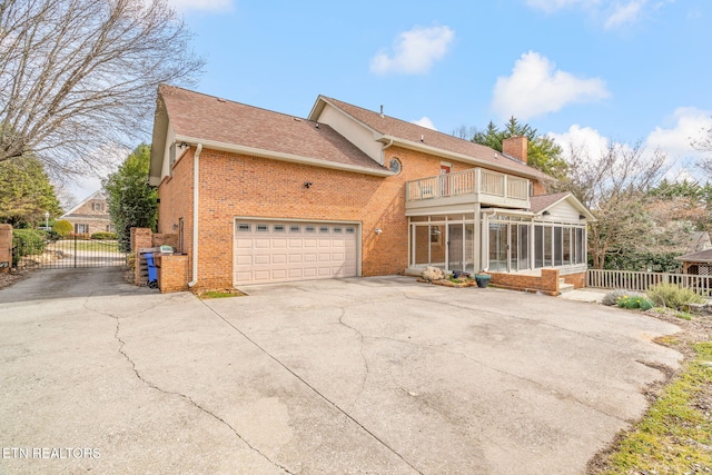 rear view of property featuring brick siding, a gate, a sunroom, a balcony, and a chimney