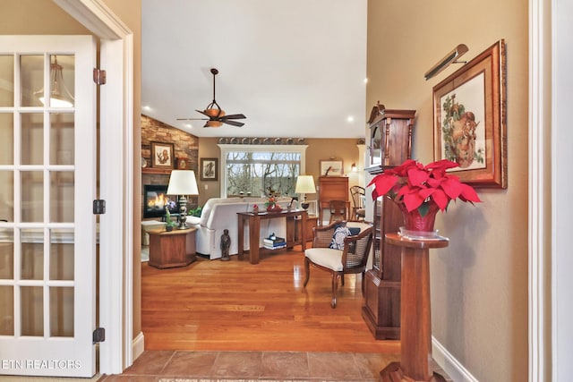 foyer featuring hardwood / wood-style flooring, vaulted ceiling, a stone fireplace, and ceiling fan