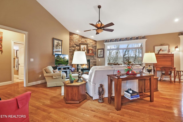 living room featuring light hardwood / wood-style flooring, a stone fireplace, vaulted ceiling, and ceiling fan