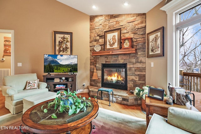 living room with a stone fireplace, wood-type flooring, and vaulted ceiling