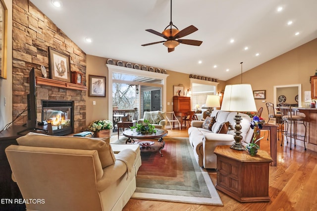 living room featuring ceiling fan, lofted ceiling, a stone fireplace, and light hardwood / wood-style floors