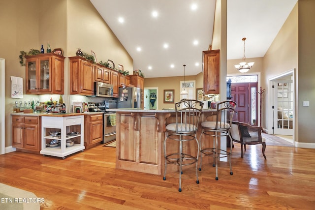 kitchen featuring an inviting chandelier, high vaulted ceiling, hanging light fixtures, light hardwood / wood-style flooring, and stainless steel appliances