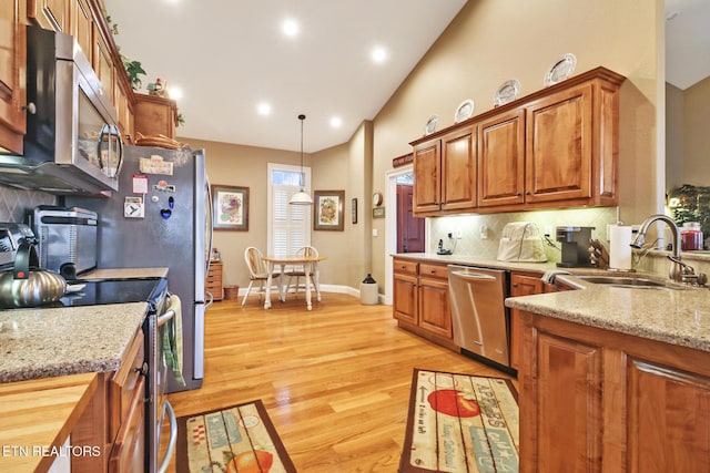 kitchen featuring appliances with stainless steel finishes, decorative light fixtures, sink, decorative backsplash, and light hardwood / wood-style floors