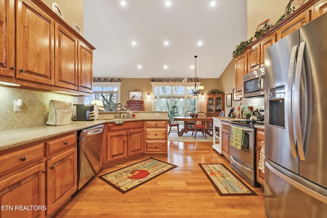 kitchen with sink, light wood-type flooring, appliances with stainless steel finishes, pendant lighting, and backsplash