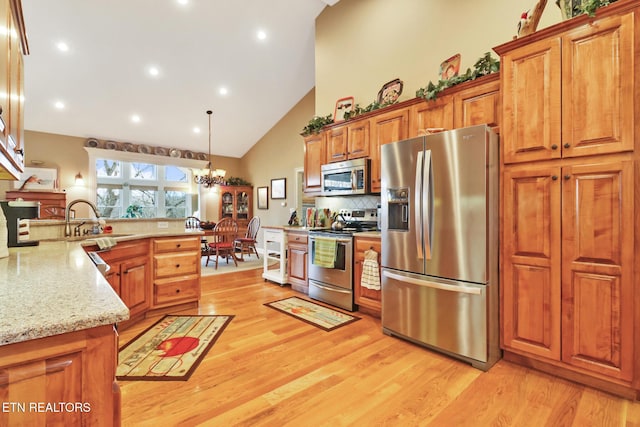 kitchen with decorative light fixtures, sink, stainless steel appliances, light stone countertops, and light wood-type flooring