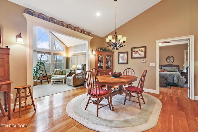 dining room with wood-type flooring, high vaulted ceiling, and an inviting chandelier