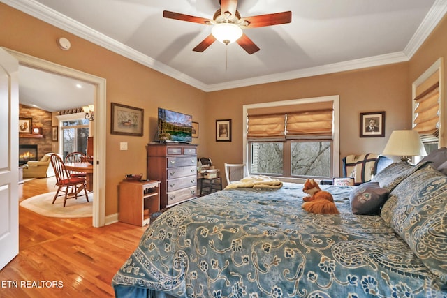 bedroom featuring hardwood / wood-style floors, crown molding, a stone fireplace, and ceiling fan