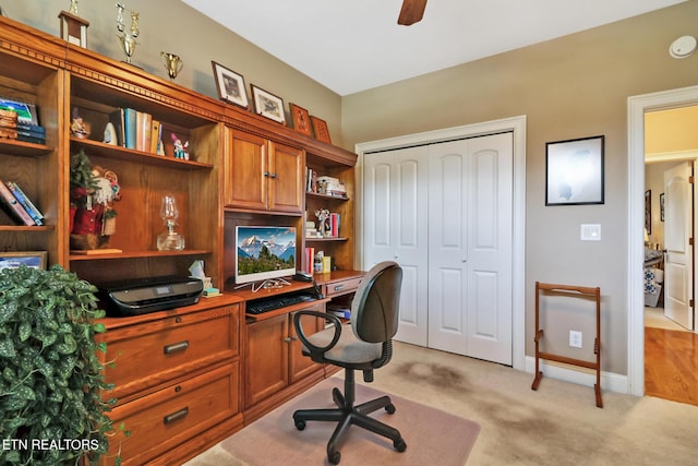 carpeted home office with built in desk and ceiling fan