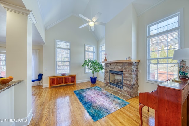 living room with a stone fireplace, light hardwood / wood-style flooring, high vaulted ceiling, and ceiling fan