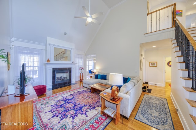 living room with a fireplace, wood-type flooring, ornamental molding, and ceiling fan